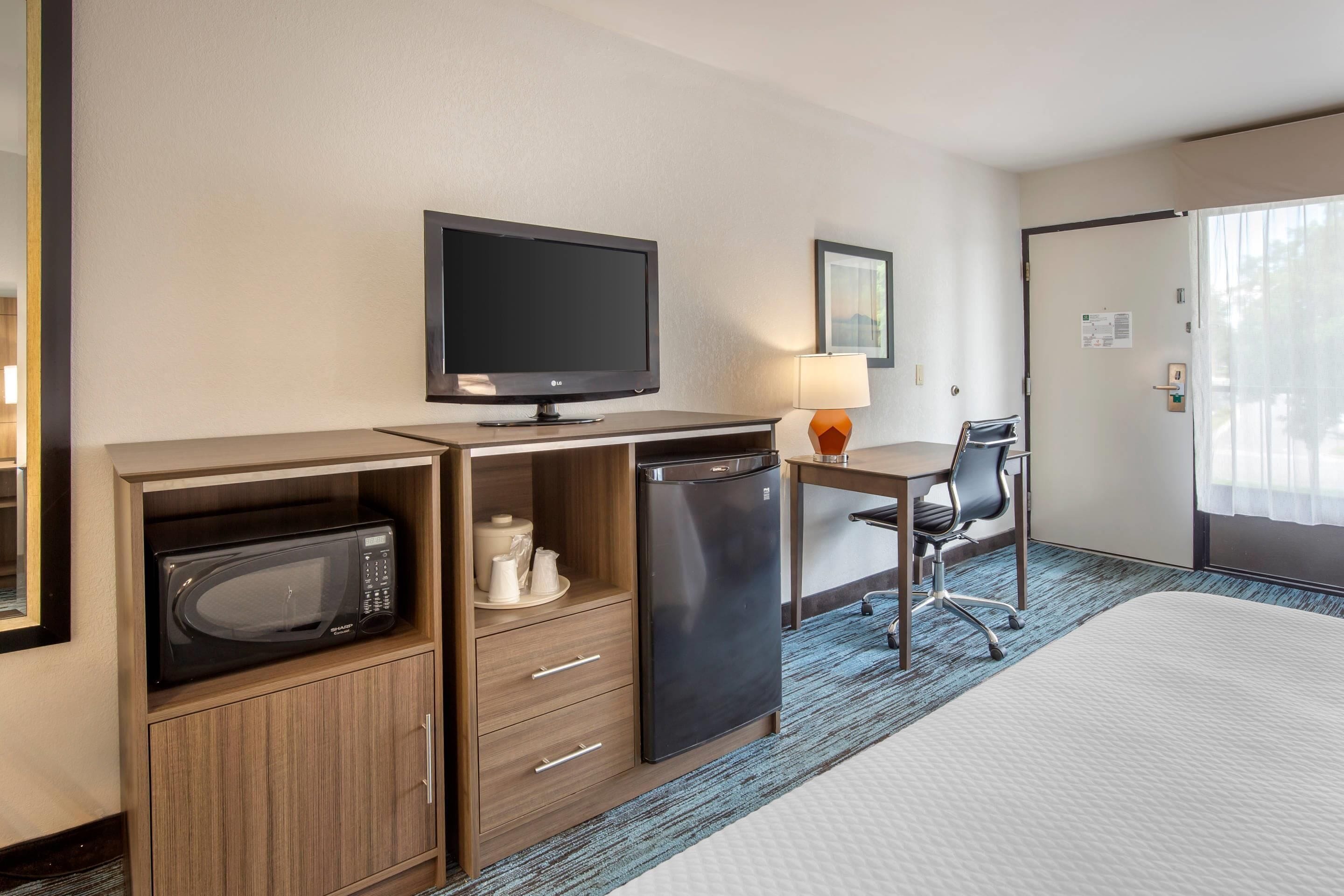 Een hotelkamer met een bed, een bureau met stoel, een televisie, een magnetron en een koelkast.