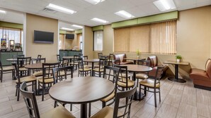 A dining area with multiple tables and chairs, a television mounted on the wall, and a kitchen area in the background. - Quality Inn Mount Airy Mayberry (Mount Airy)