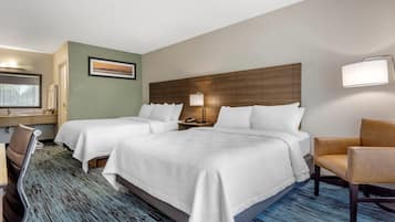 A hotel room with two beds, a desk with a chair, a lamp, and a painting on the wall.