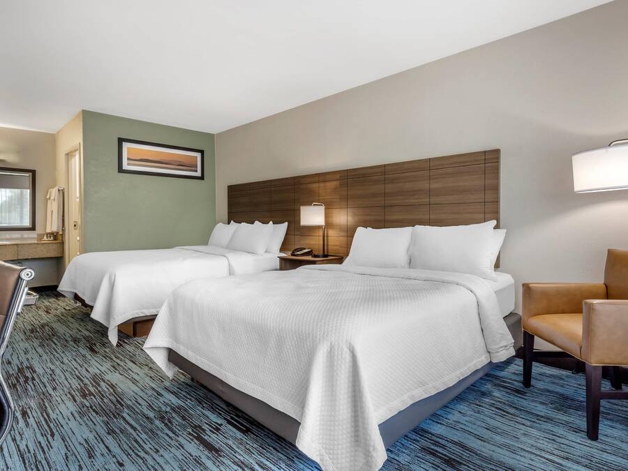 A hotel room with two beds, a desk with a chair, a lamp, and a painting on the wall.