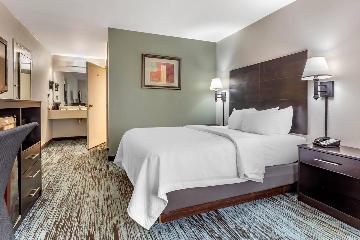 Una habitación de hotel con una cama, lámparas de noche, un escritorio y un espejo.