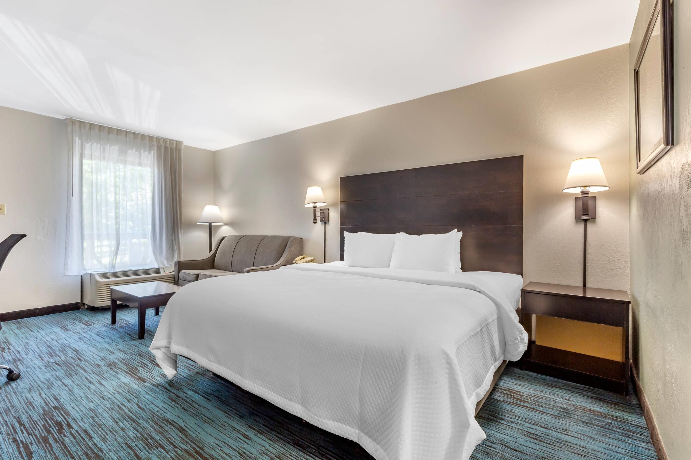 A hotel room with a large bed, two bedside tables, a chair, a desk, and a window with curtains.