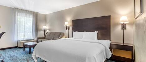 A hotel room with a large bed, two bedside tables, a chair, a desk, and a window with curtains.