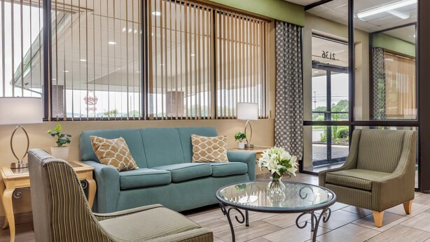A modern living room with a sofa, armchairs, a glass coffee table, and a side table with a lamp. - Quality Inn Mount Airy Mayberry (Mount Airy)