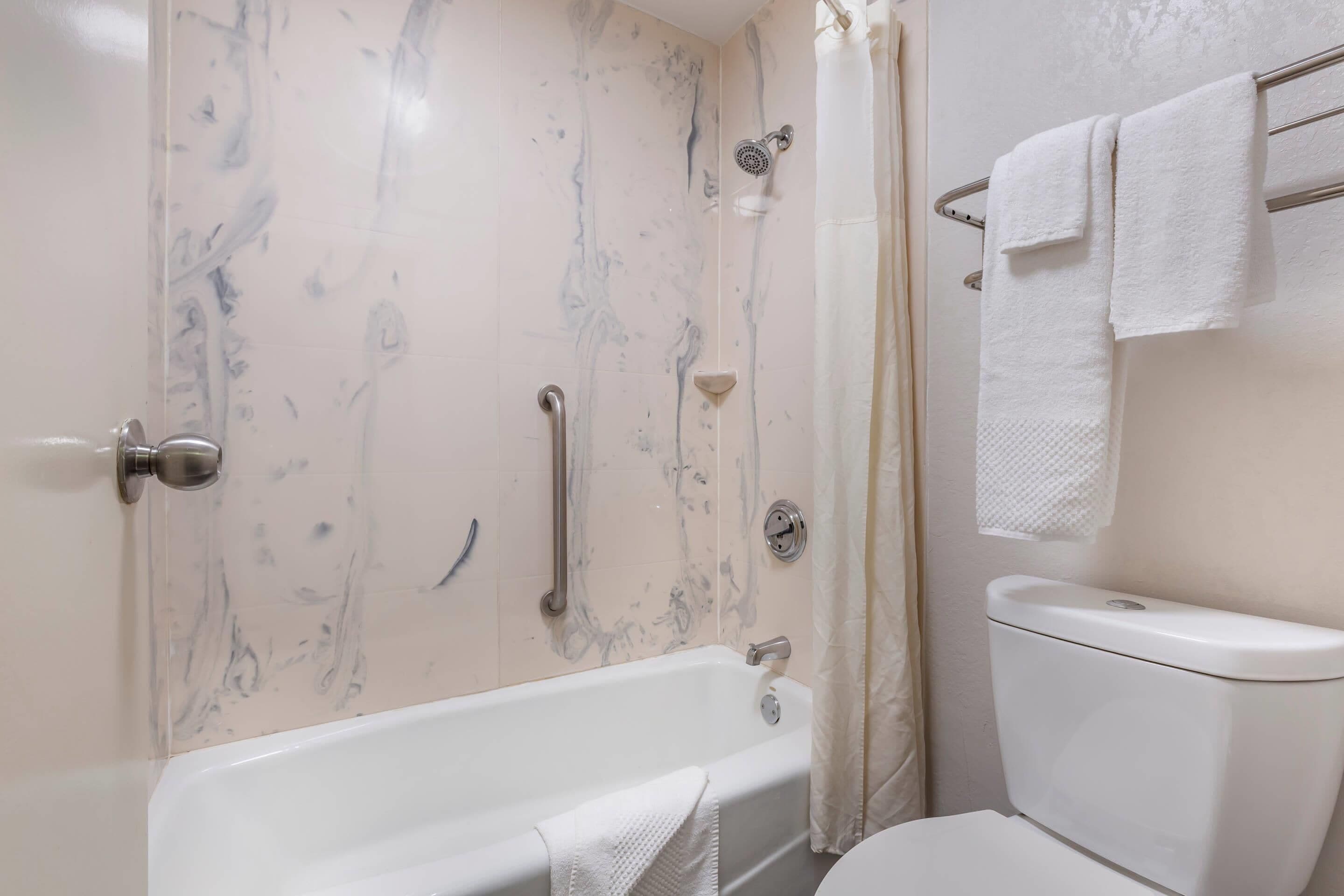 Un baño con bañera, inodoro y barras de apoyo.