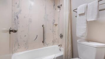 A bathroom with a bathtub, toilet, and handrails.
