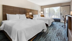 A hotel room with two beds, a large wooden headboard, a desk with a chair, and a large window with curtains. - Quality Inn Mount Airy Mayberry (Mount Airy)