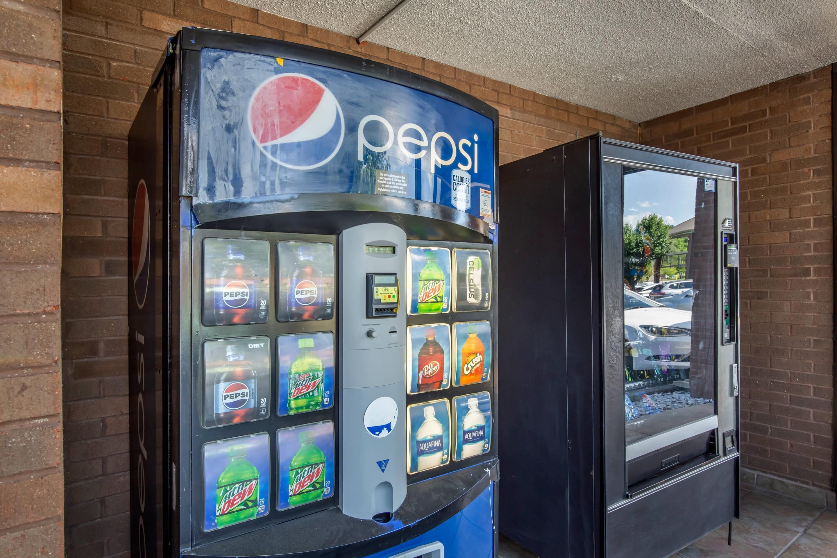 Un distributeur automatique de boissons, notamment de Pepsi, situé à côté d’une vitrine.