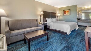 A hotel room with a bed, a sofa, a nightstand, a lamp, and a mirror. - Quality Inn Mount Airy Mayberry (Mount Airy)
