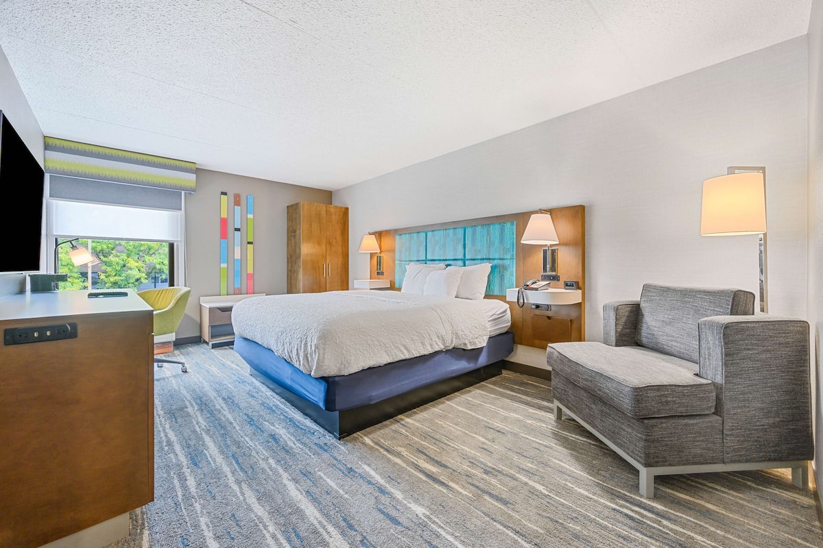 A hotel room with a bed, a desk, a chair, and a TV.