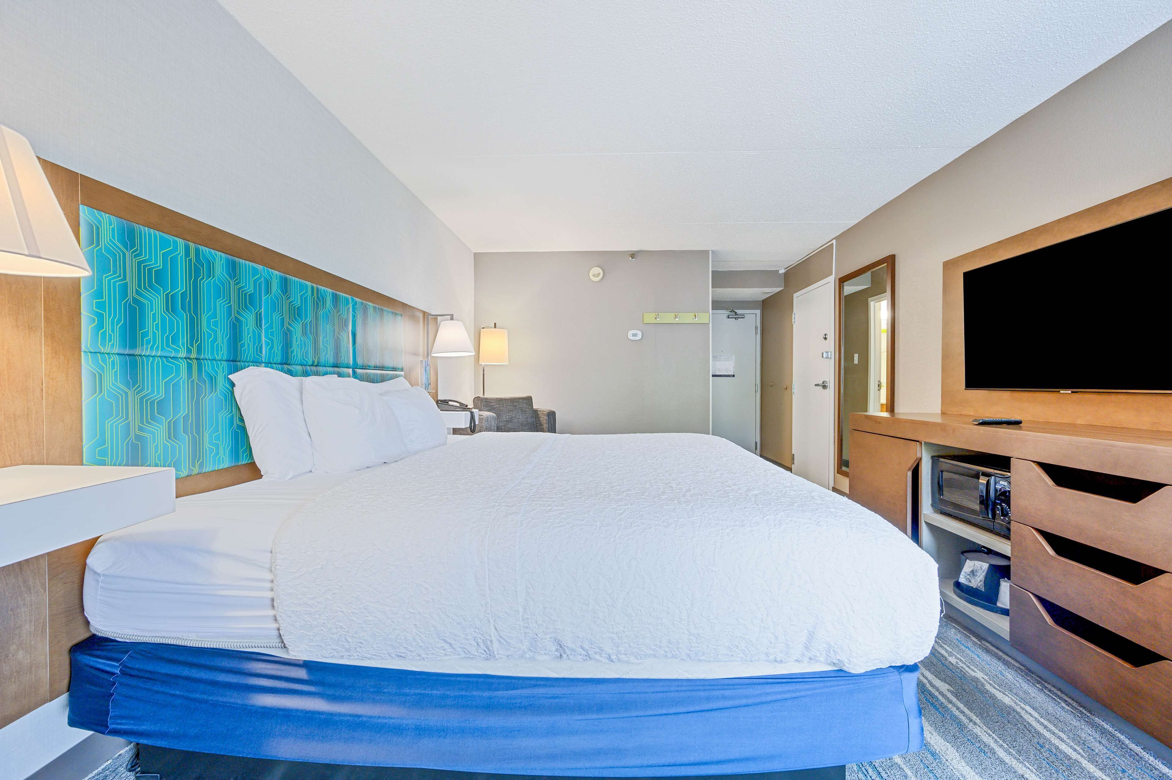 Habitación de hotel con una cama grande, televisor de pantalla plana, cabecero de madera y escritorio con lámpara.