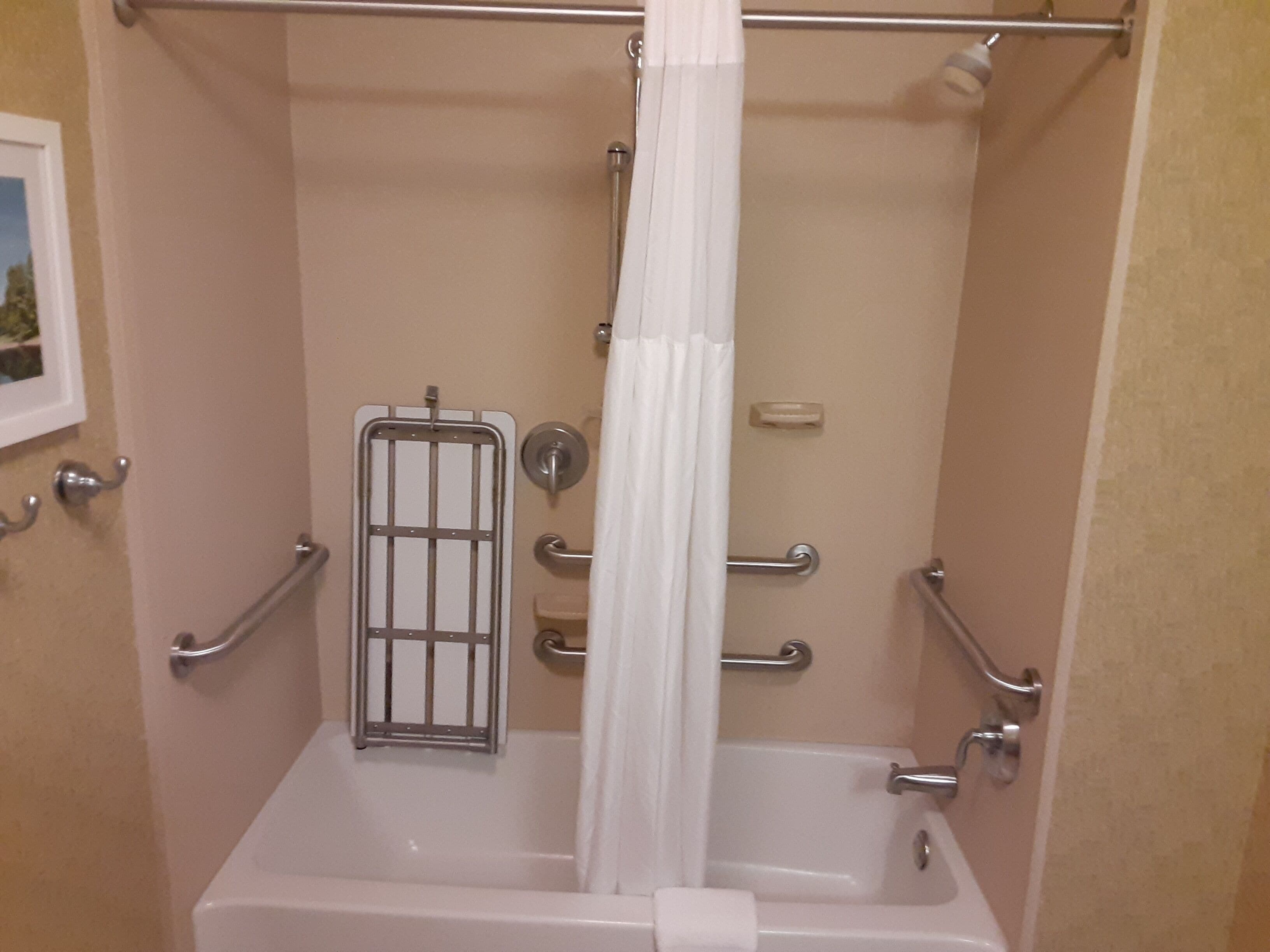 Un baño con bañera, barras de apoyo, cortina de ducha y un toallero.