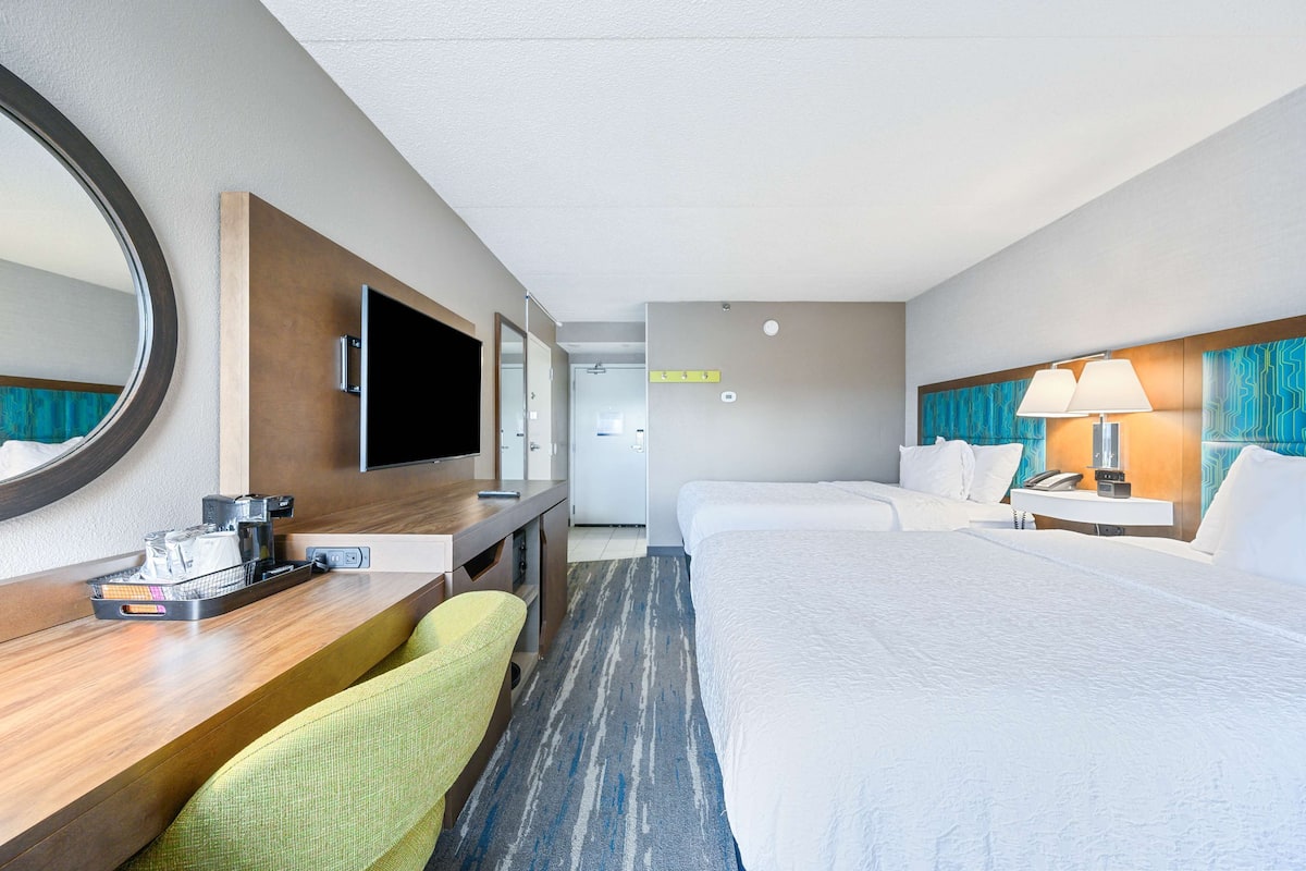 A hotel room with a bed, a desk with a chair, a TV, and a lamp.