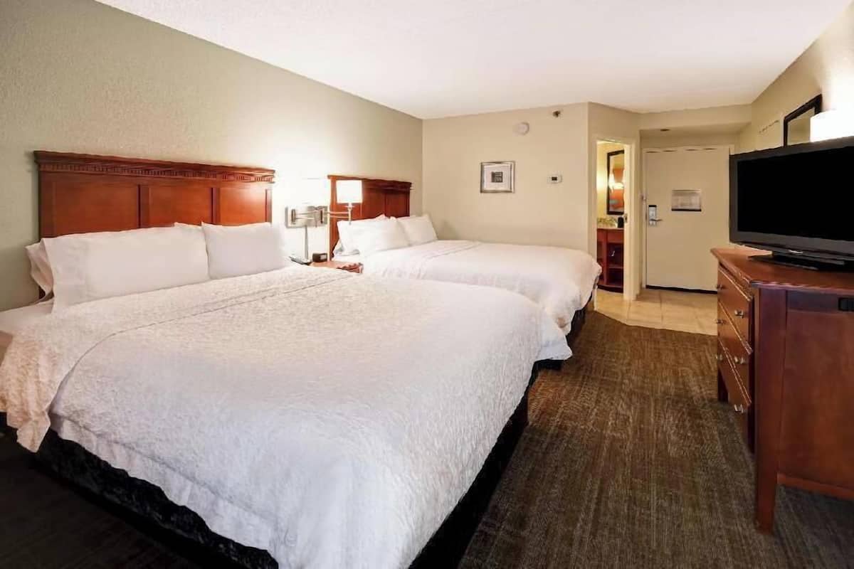 A hotel room with two beds, a television, a dresser, and a door leading to a bathroom.
