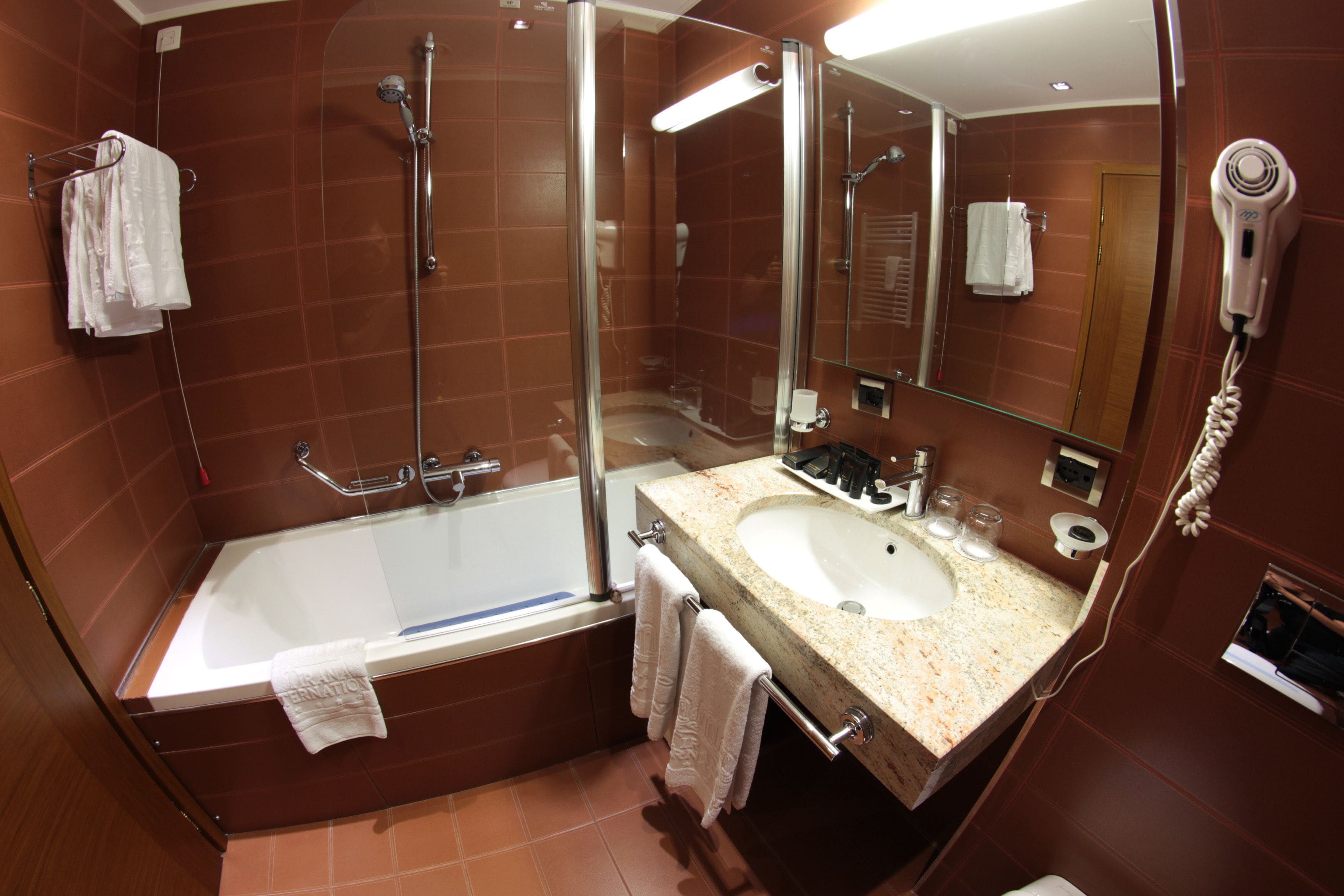 A modern bathroom with a glass-enclosed shower, a large sink, and a hairdryer mounted on the wall.