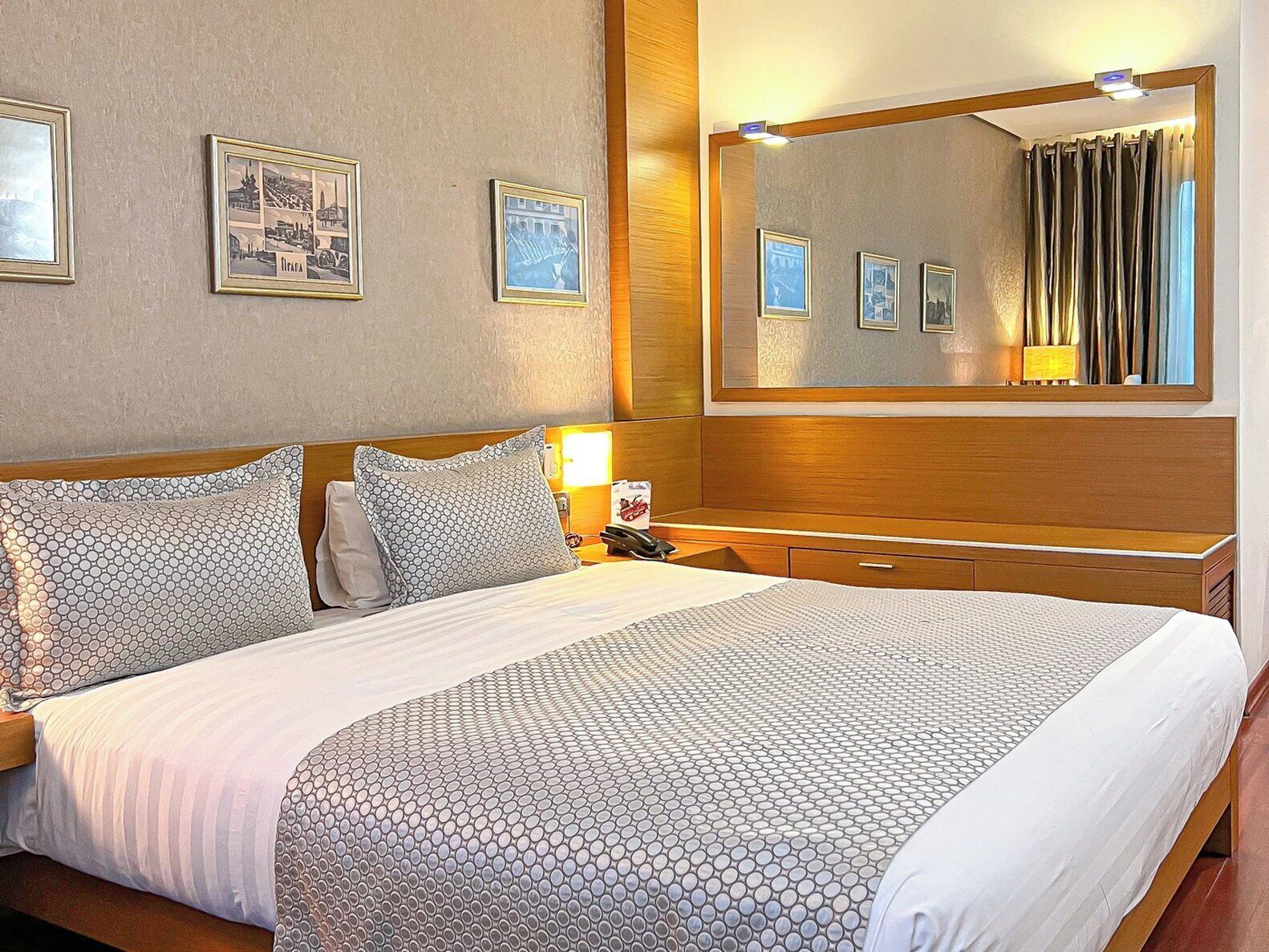 Une chambre d’hôtel avec un grand lit, une tête de lit en bois, une table de chevet avec une lampe et un miroir fixé au mur.