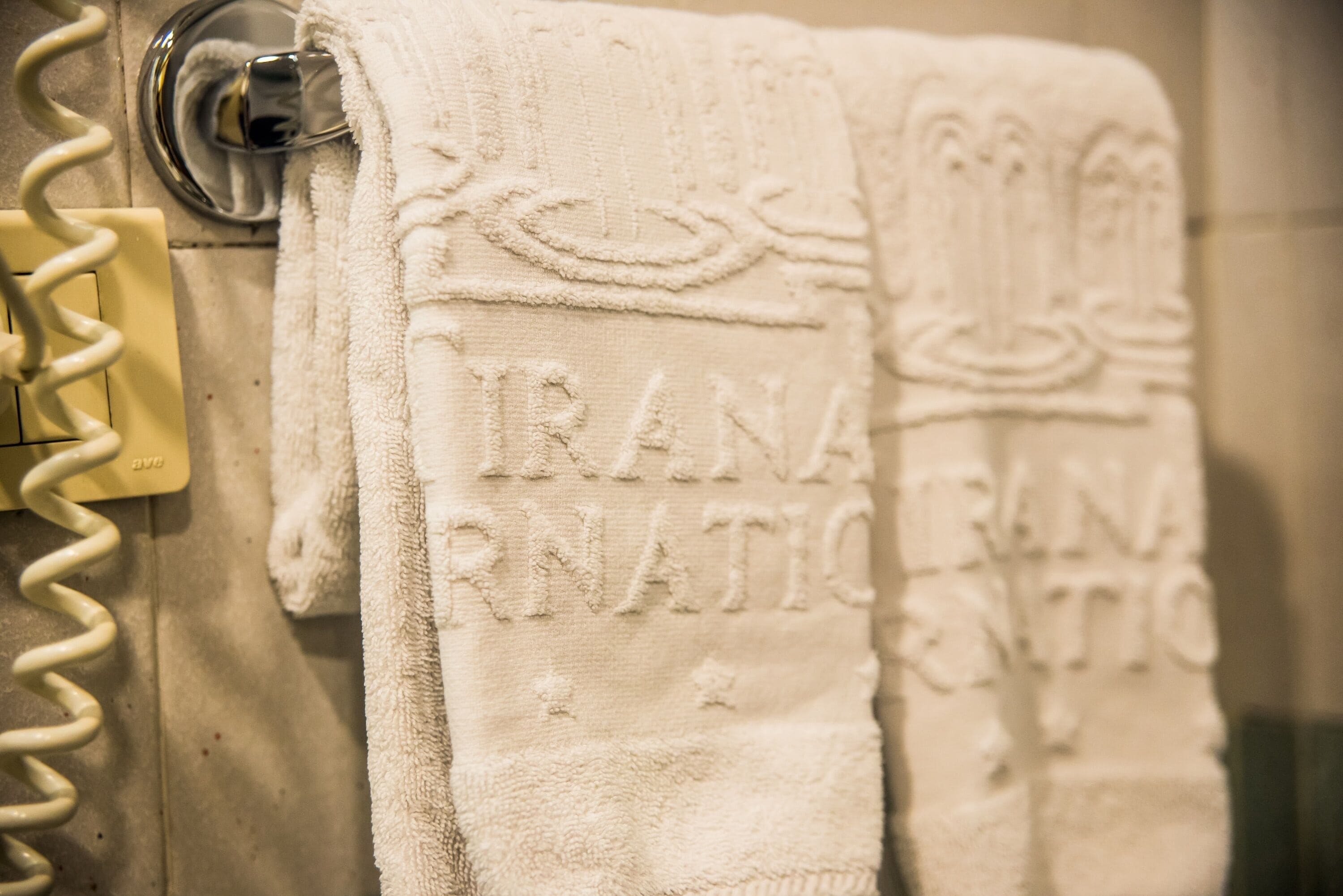 Un baño con dos toallas colgadas en un perchero, una con la etiqueta 'IRANIAN' y la otra con 'IRANIAN'.