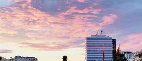 Un paisaje urbano que muestra un edificio grande, una estatua y un parque con gente.