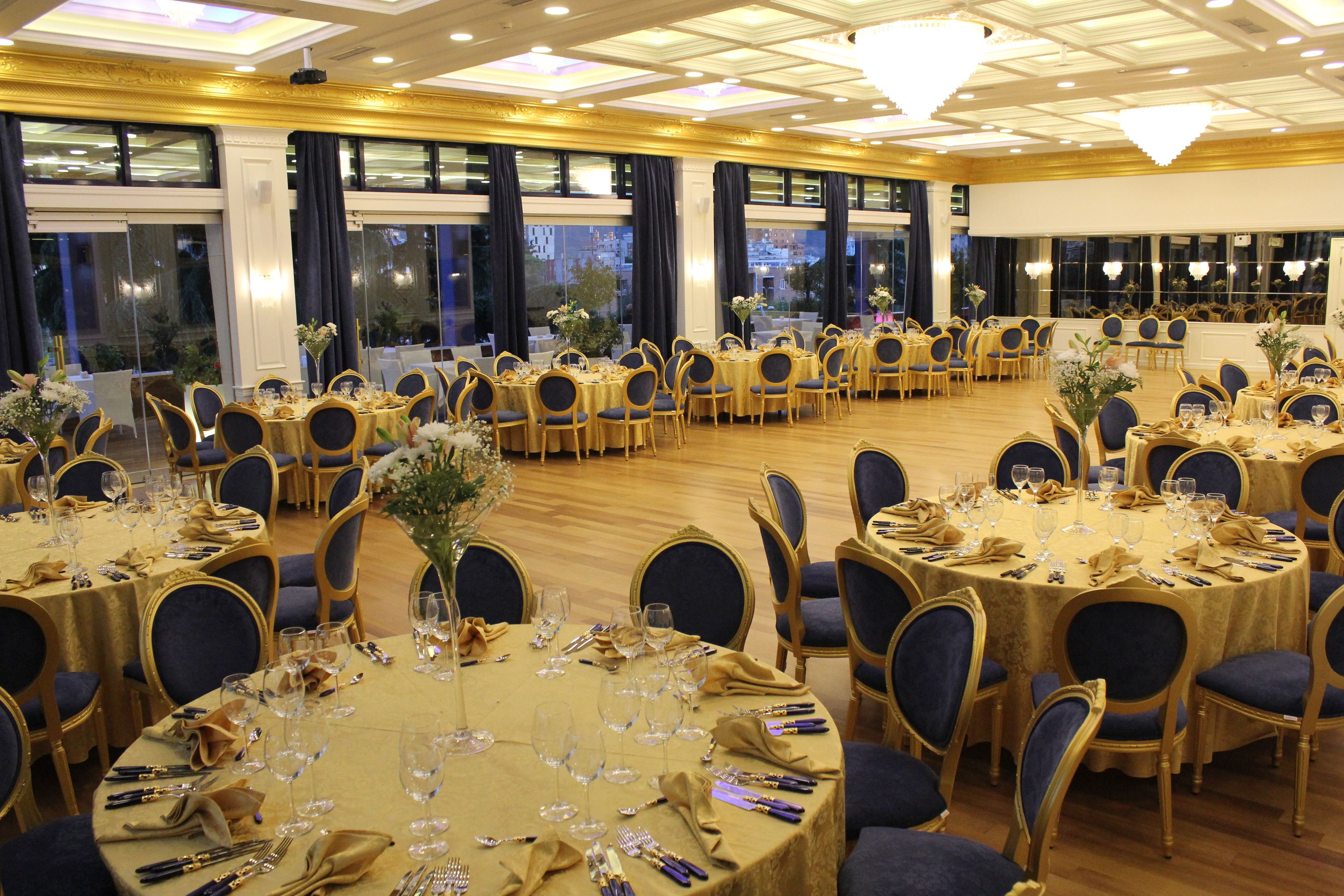 A banquet hall with round tables set for dining, featuring gold tablecloths and blue chairs.