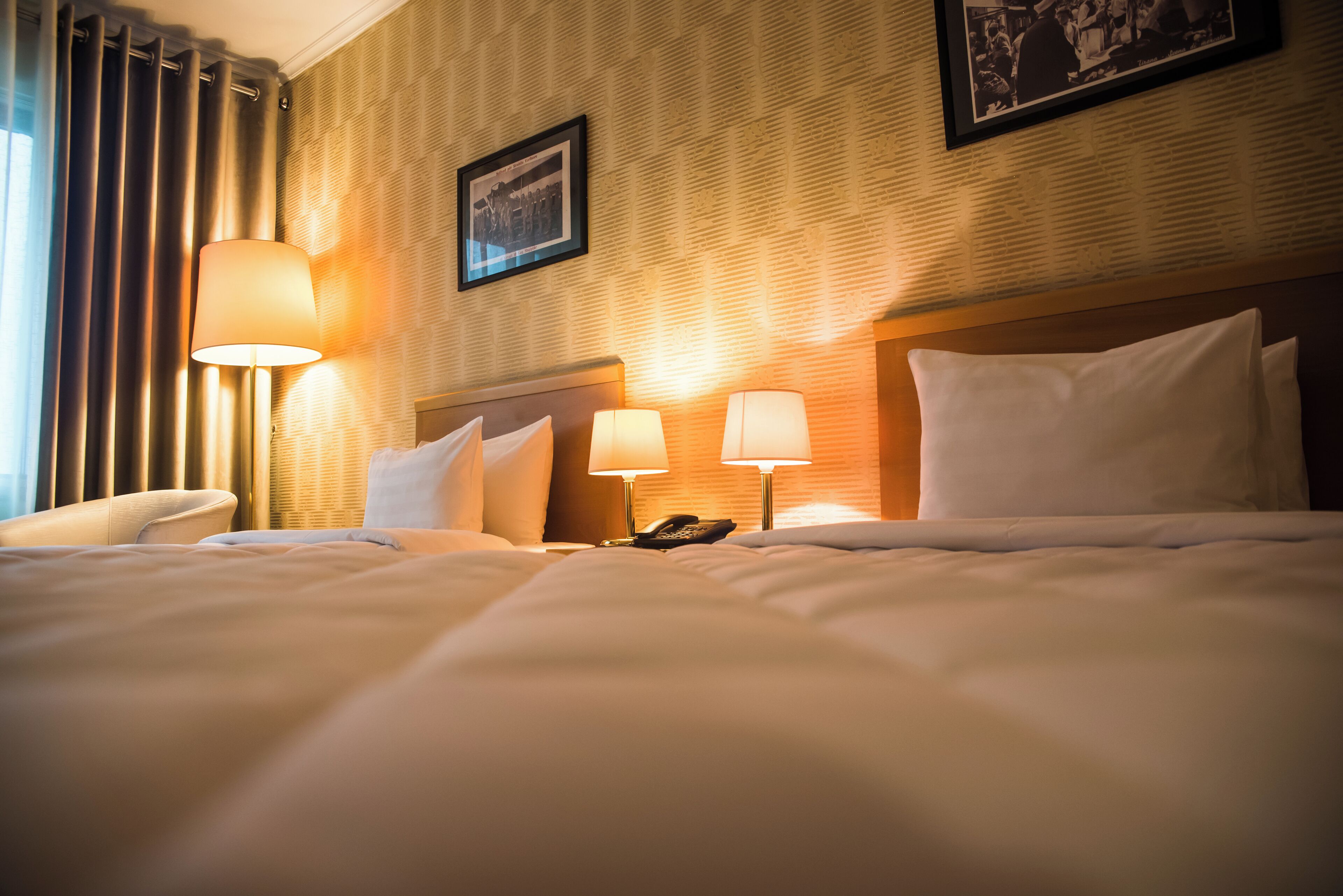 A hotel room with a neatly made bed, two bedside lamps, a telephone, and a framed picture on the wall.