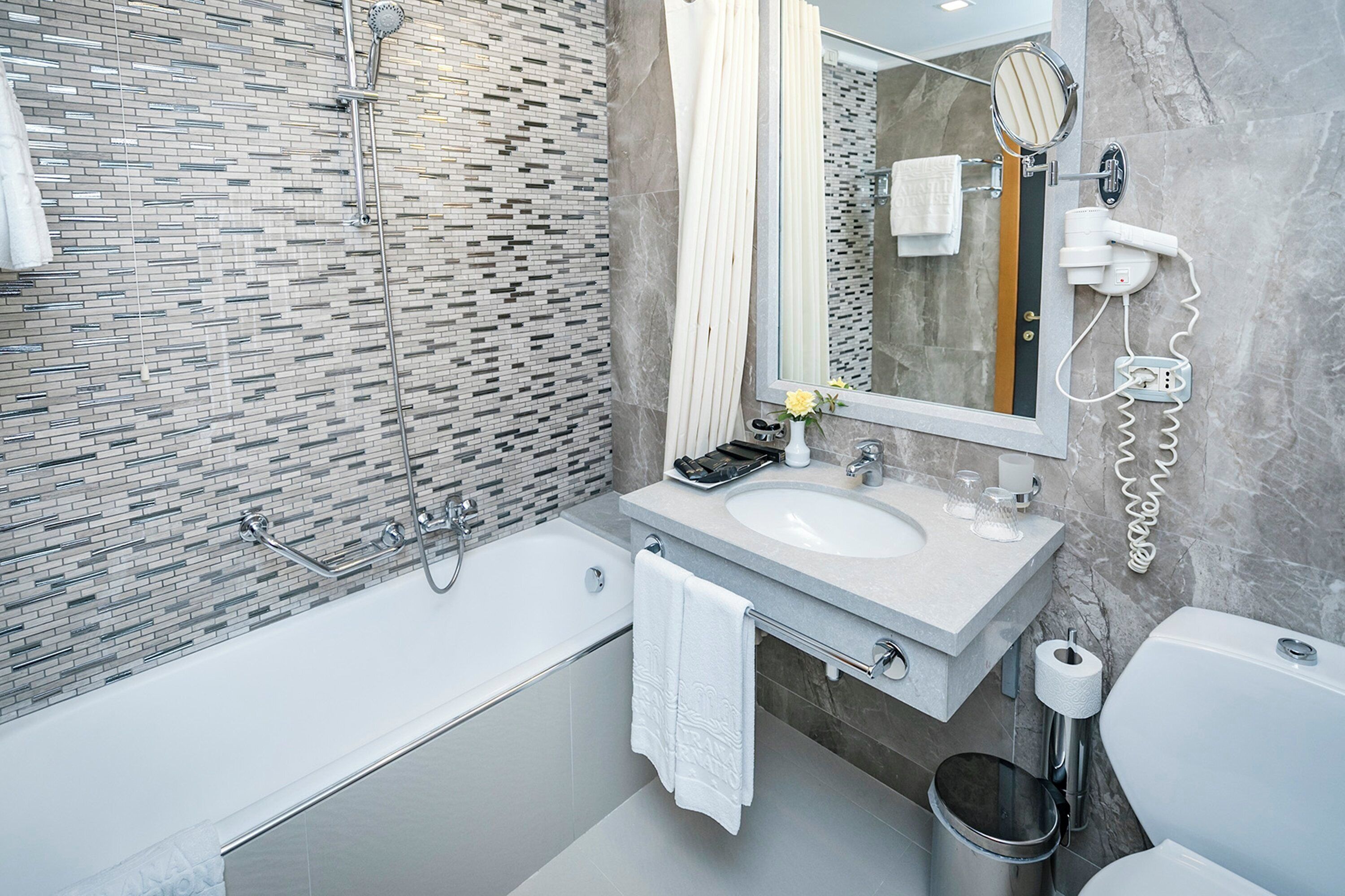 A modern bathroom with a tiled shower wall, a large mirror, a sink with a vanity, and a toilet.