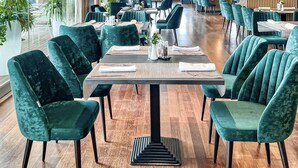 Un vaste espace dédié à la salle à manger, avec des chaises à l’assise verte, une table centrale dressée pour le repas et de grandes fenêtres laissant entrer la lumière naturelle.