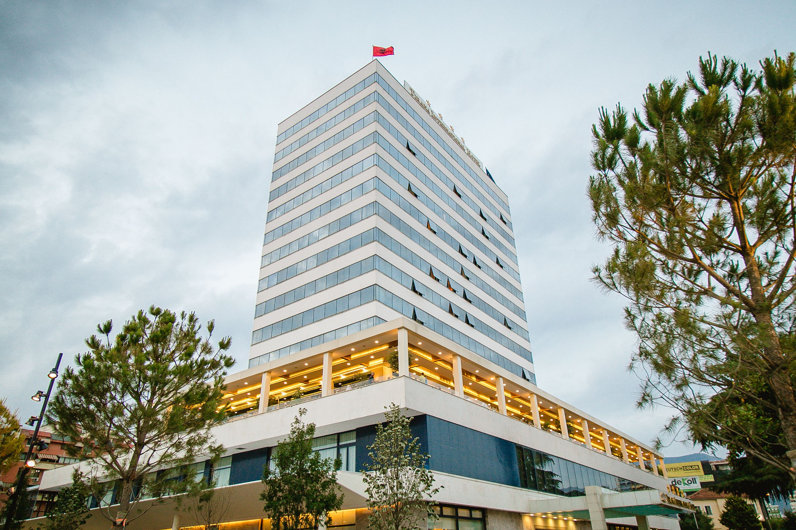 A tall, modern hotel with a distinctive red flag on top, featuring multiple floors and a prominent lower section with illuminated balconies.