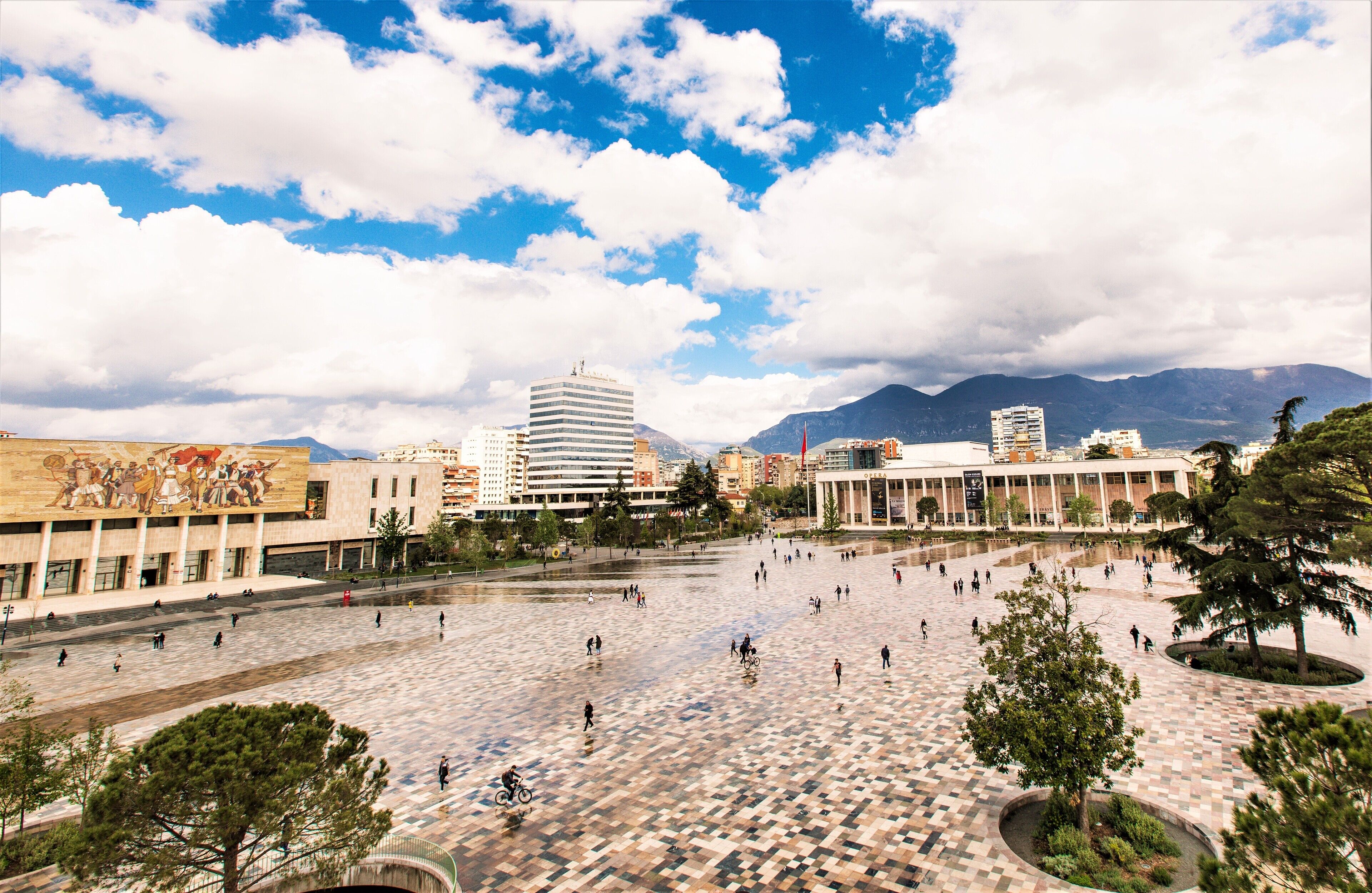 A spacious public square with a tiled floor, surrounded by buildings and trees.