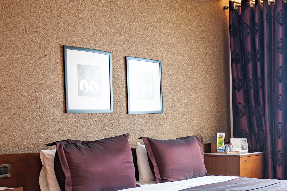 Hotellihuone, jossa on sänky, yöpöytä ja kaksi kehystettyä kuvaa seinällä.
