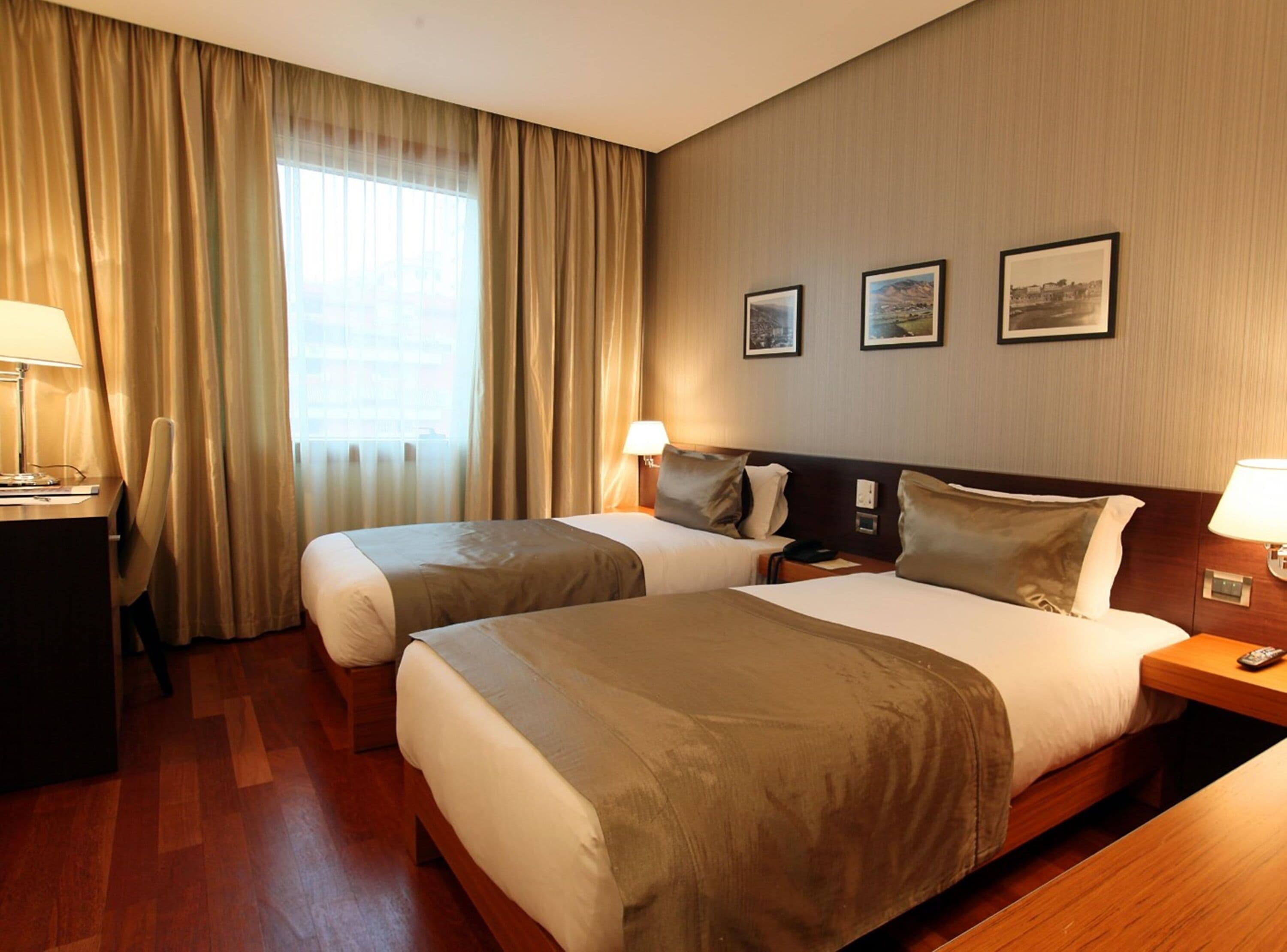 A hotel room with two beds, a desk, and a chair. There are three framed pictures on the wall.