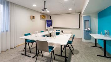 A conference room with a white table, teal chairs, a projector, and a screen.