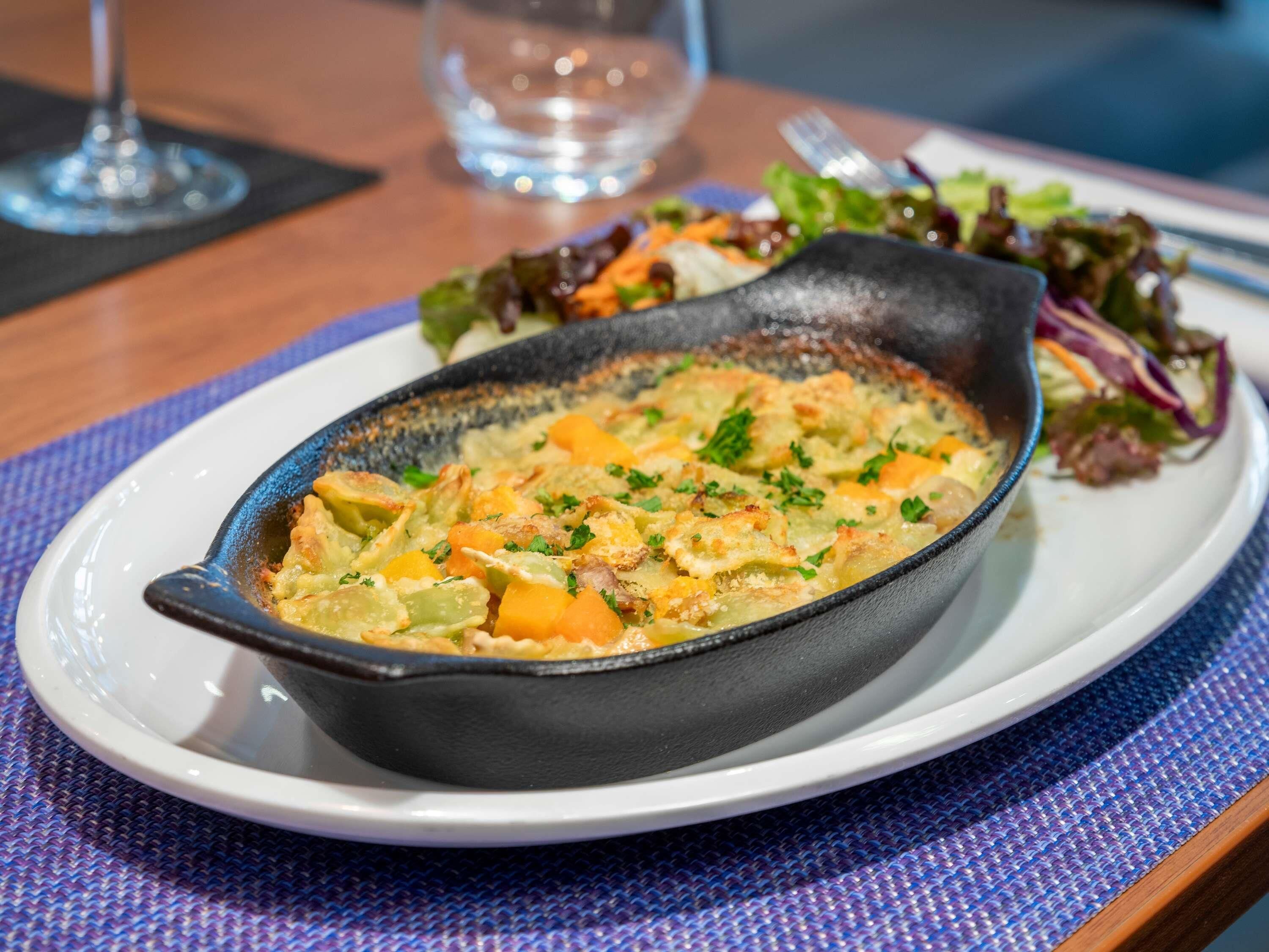 A dish in a cast iron skillet on a white plate, accompanied by a side salad.
