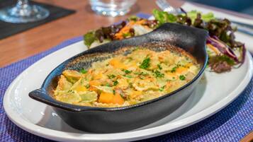 A dish in a cast iron skillet on a white plate, accompanied by a side salad.