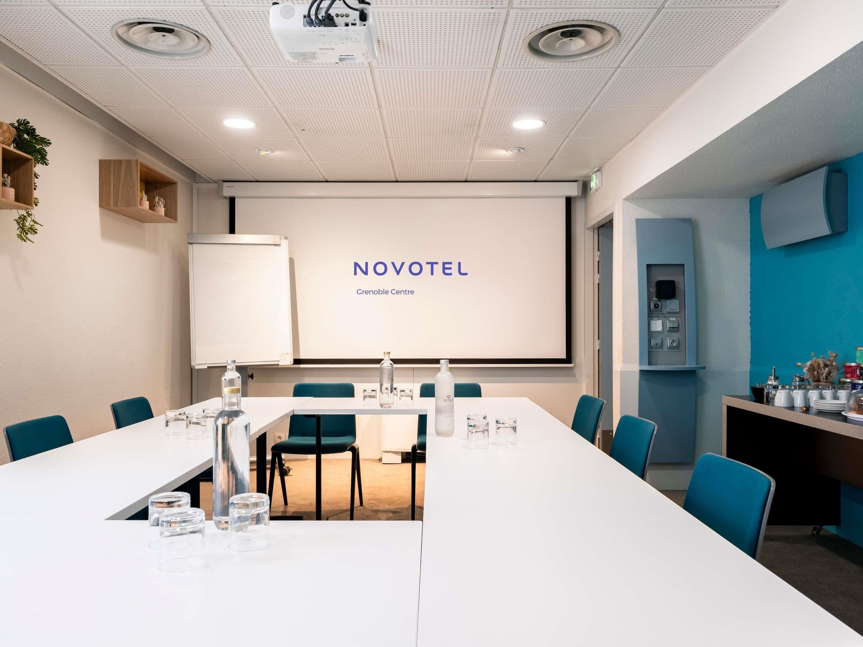 A conference room with a long table, chairs, a projector screen, and a whiteboard.