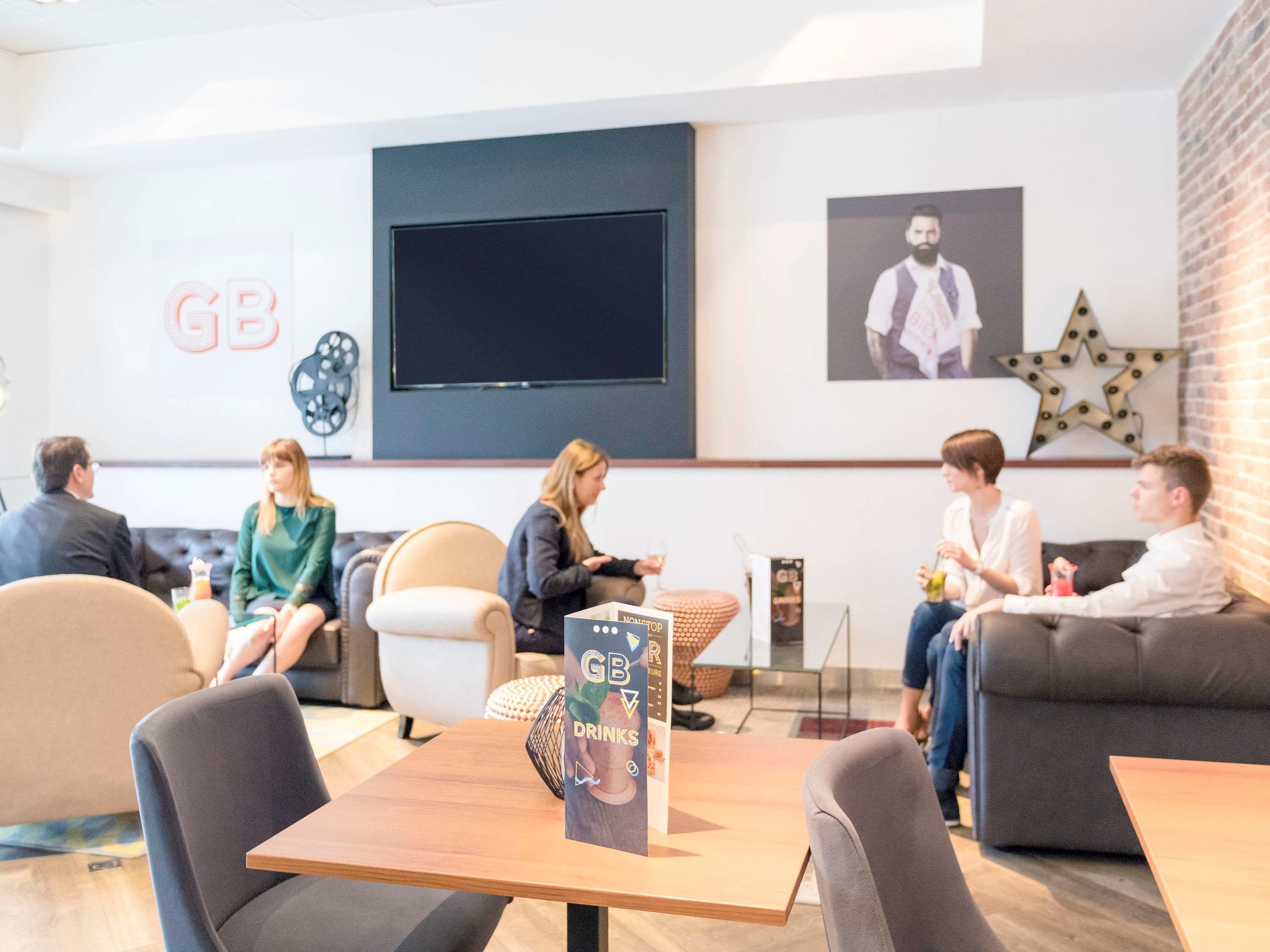 A modern lounge area with sofas and tables, a large screen, and a 'GB V' sign.
