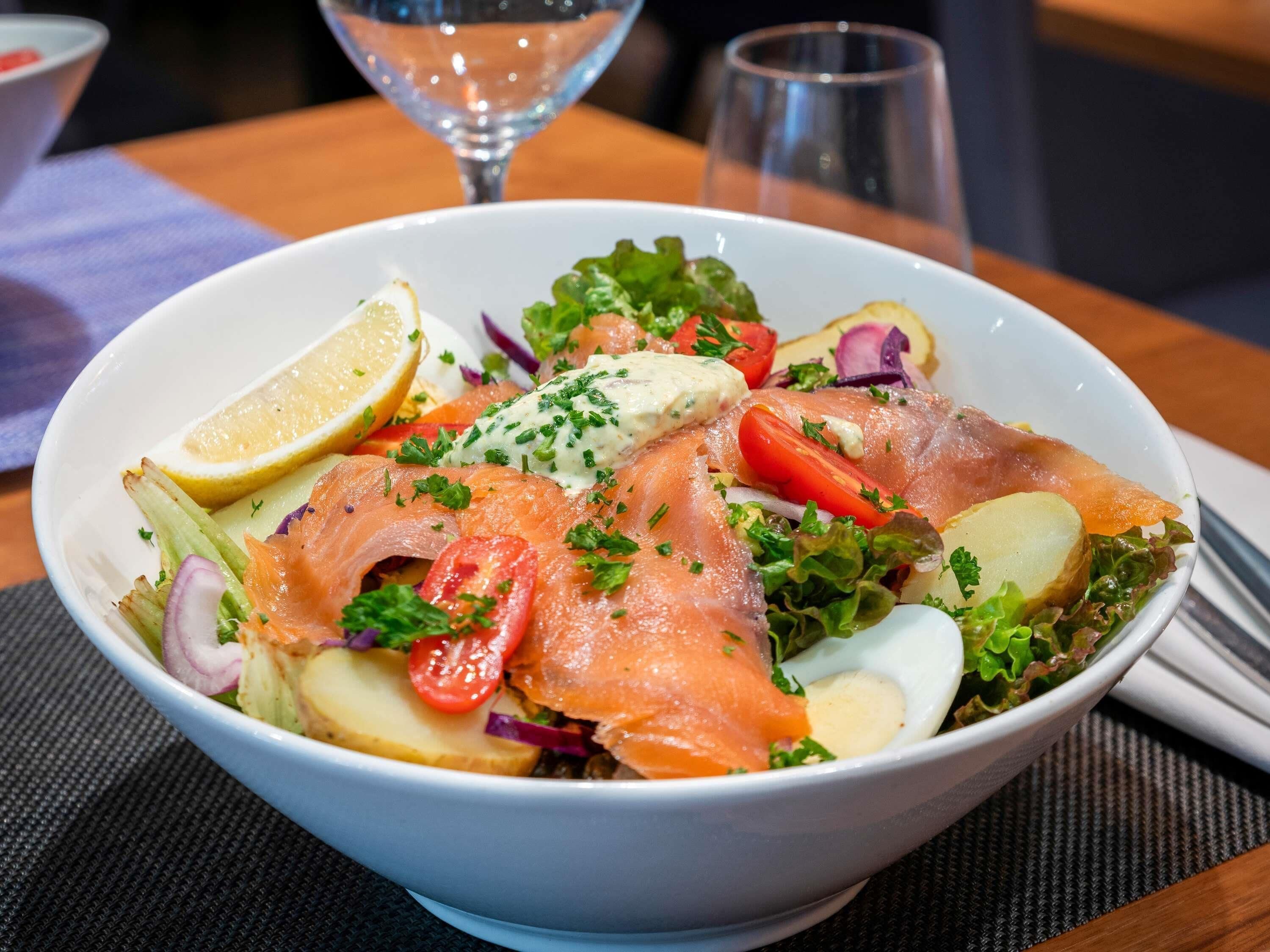 Eine Schüssel mit Essen, darunter Lachs, Gemüse und ein Zitronenschnitz.