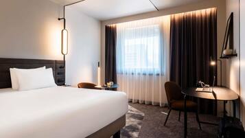 A hotel room with a large bed, a desk with a chair, a laptop, and a suitcase.