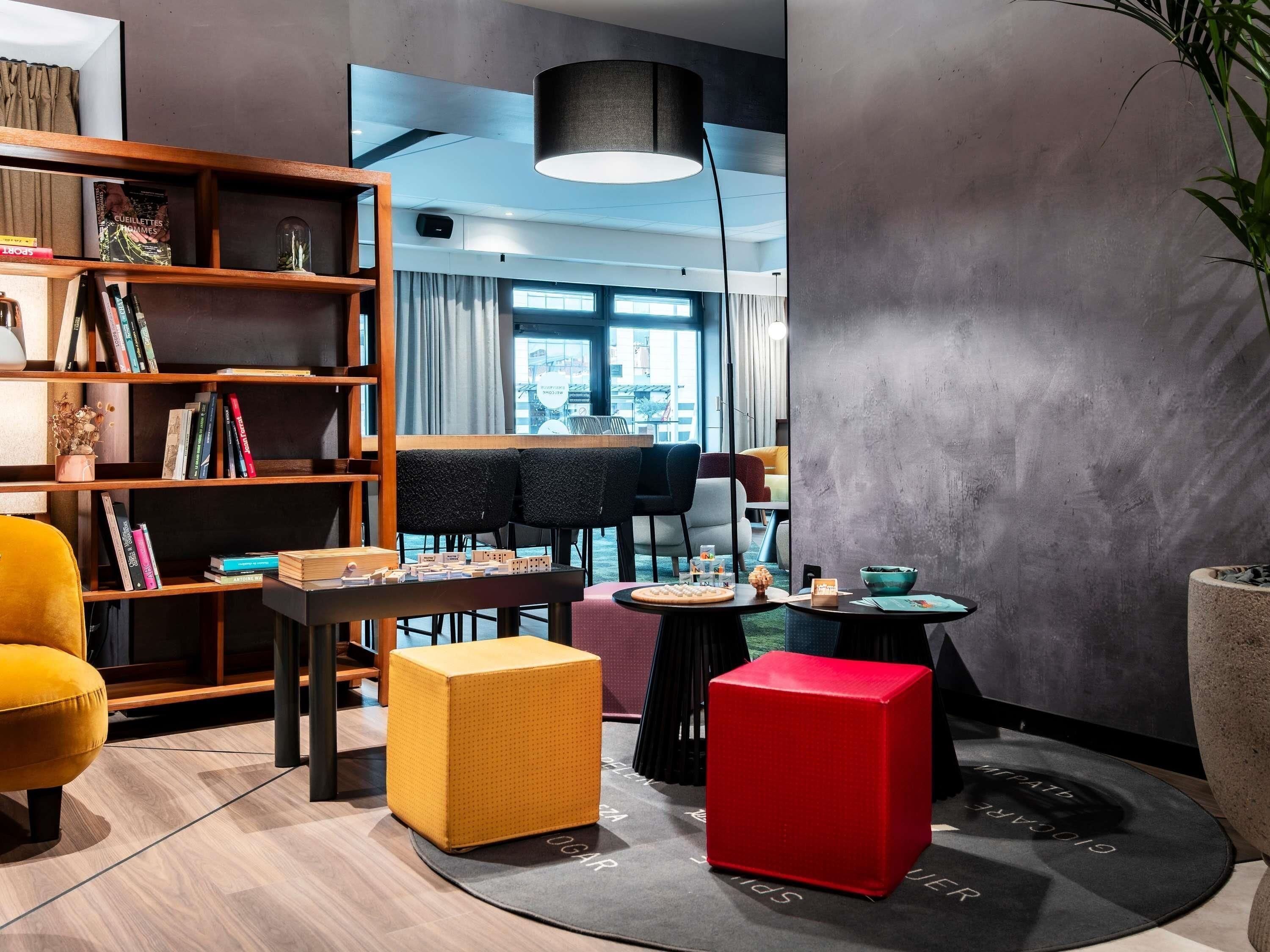 Een moderne woonkamer met een boekenkast, een eethoek en een rode accentstoel.