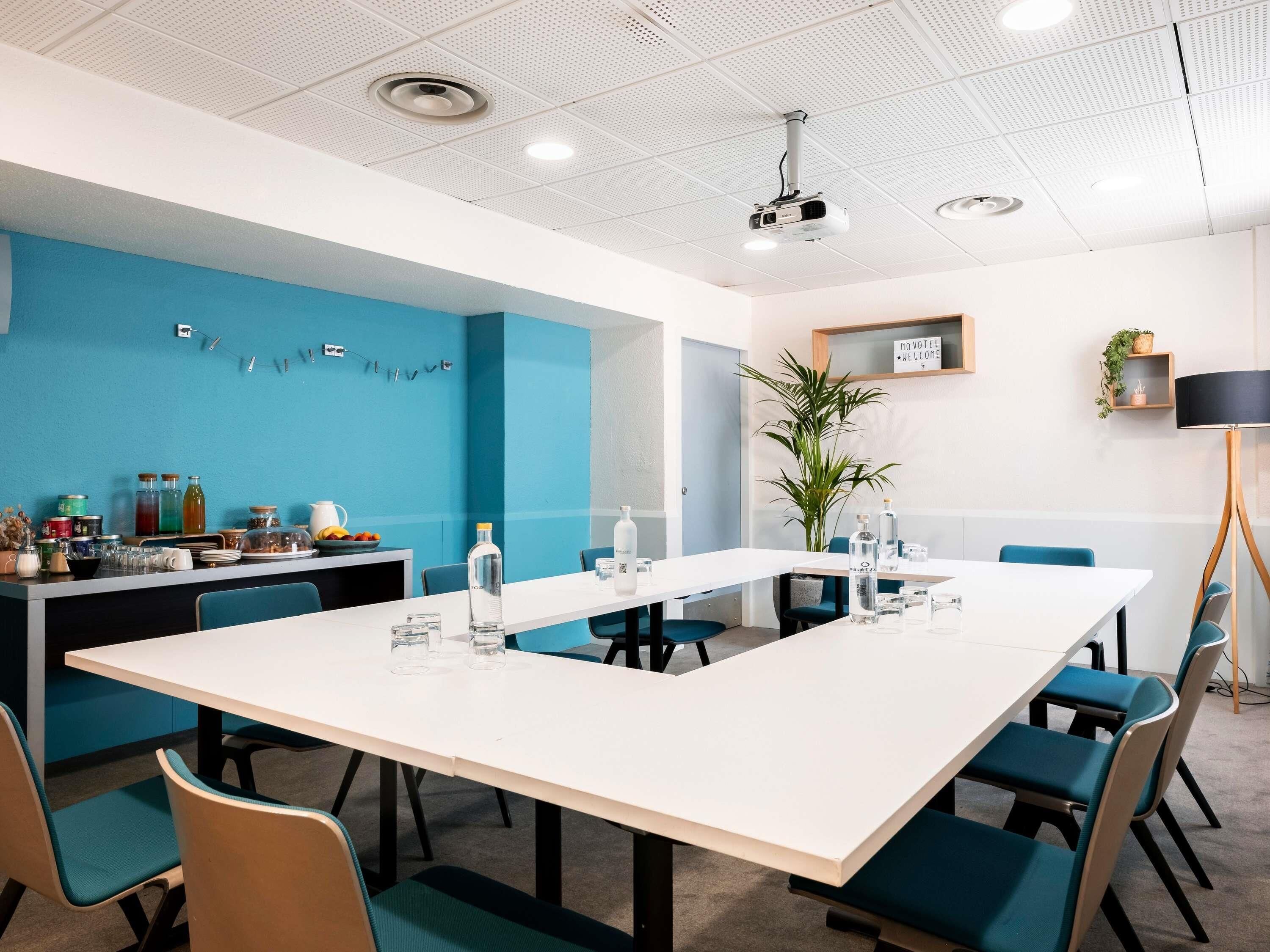 Une salle de conférence avec une longue table, des chaises, un projecteur et un panneau indiquant « Bienvenue ».