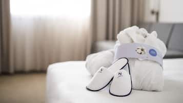 A neatly made bed with a white towel and slippers, a pillow, and a bedside table with a lamp.