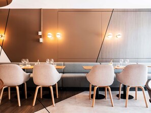 A modern dining area with a sofa and four chairs, a wooden table, and wall-mounted lighting. - Novotel Grenoble Centre (Grenoble)