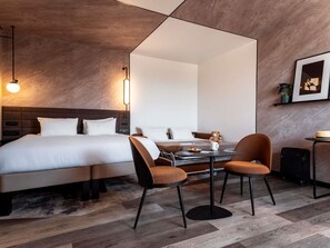 A modern hotel room with a large bed, a desk with two chairs, a mirror, and a framed picture on the wall. - Novotel Grenoble Centre (Grenoble)