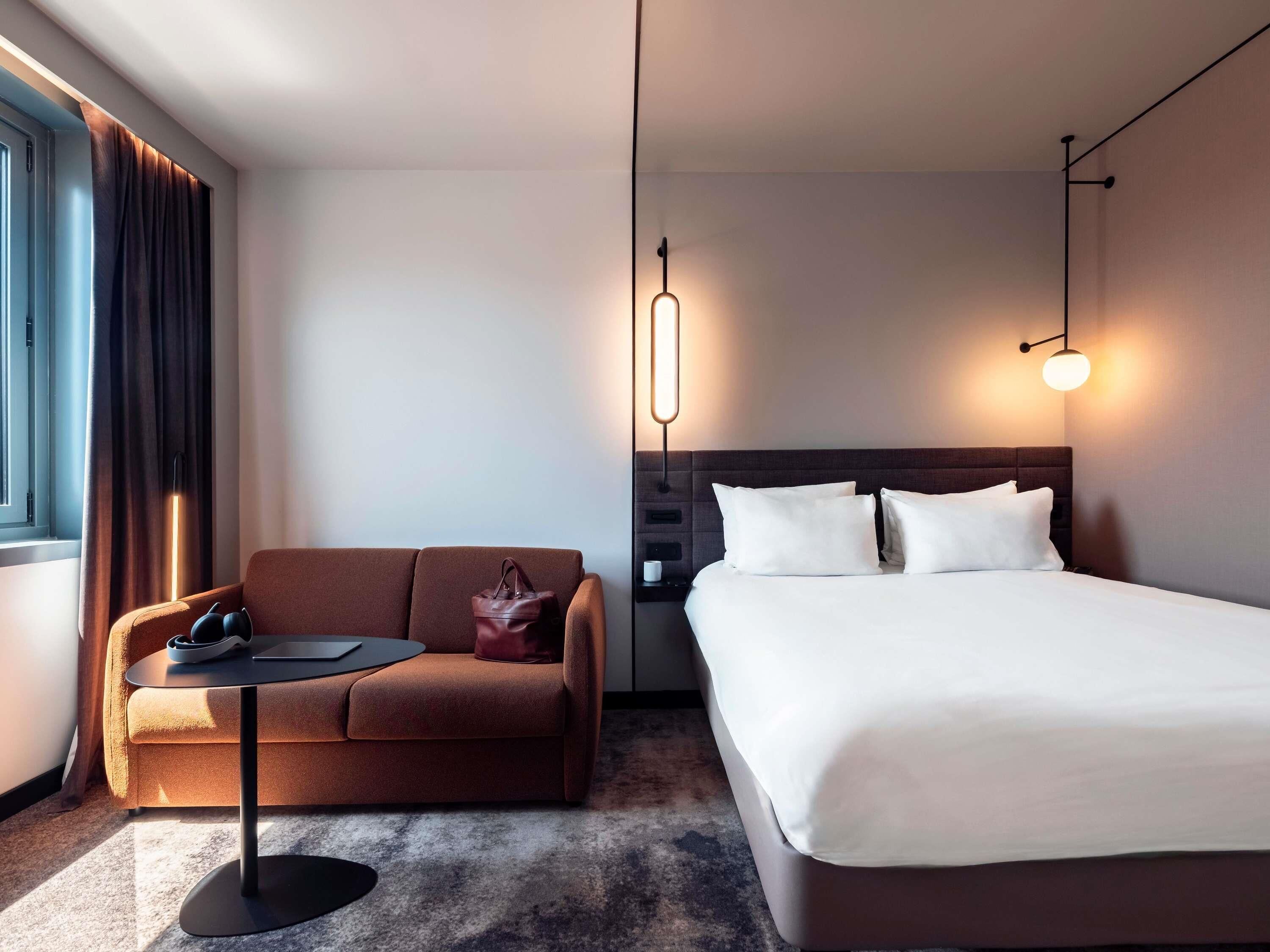 Une chambre d’hôtel moderne comprenant un lit, un canapé, une petite table et une table de chevet.