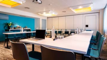 A conference room with a long table, chairs, and a projector. There are plants and water bottles on the tables.
