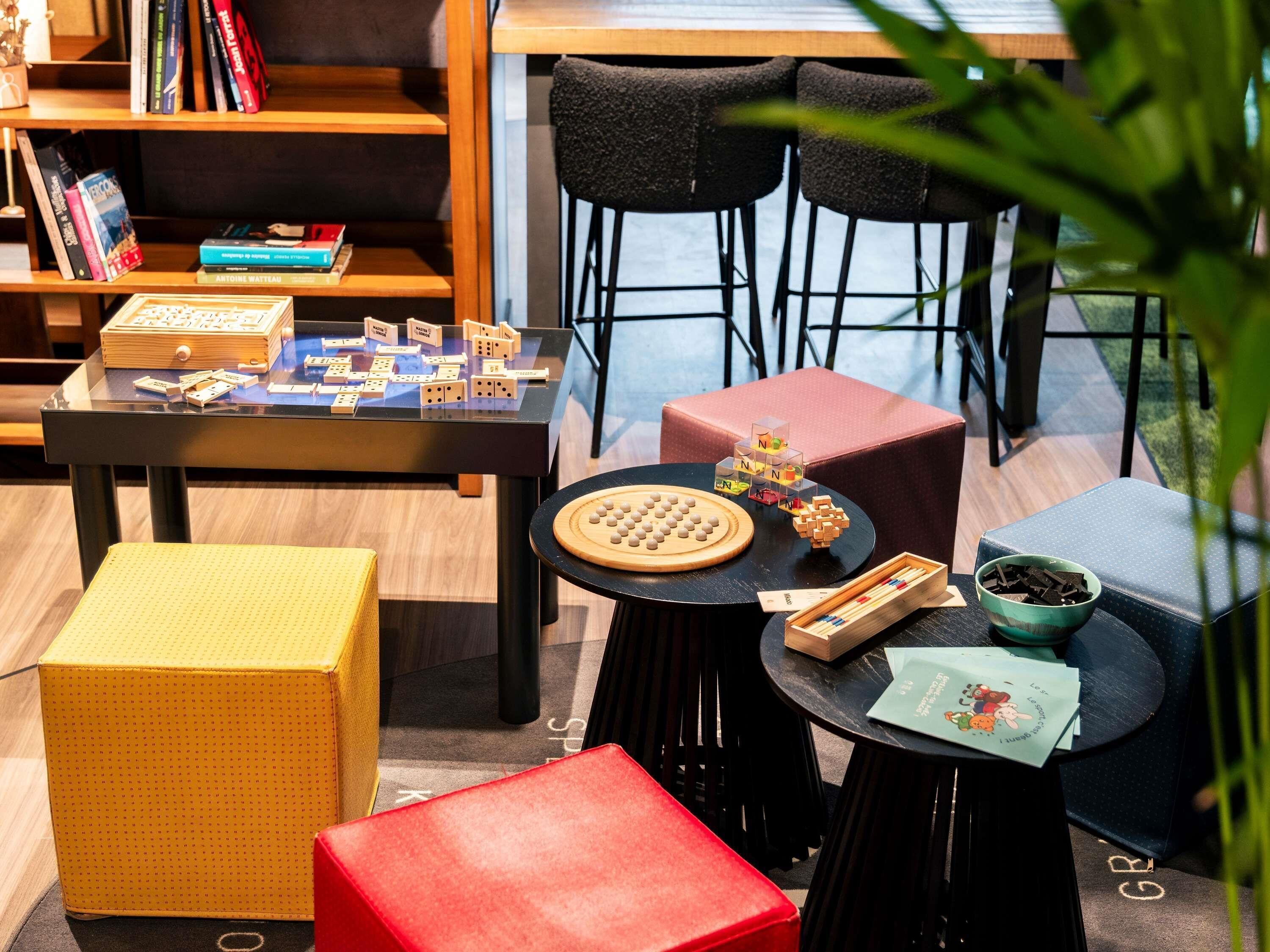 Un espace intérieur accueillant avec une table préparée pour jouer aux dominos, une petite bibliothèque et des sièges confortables.
