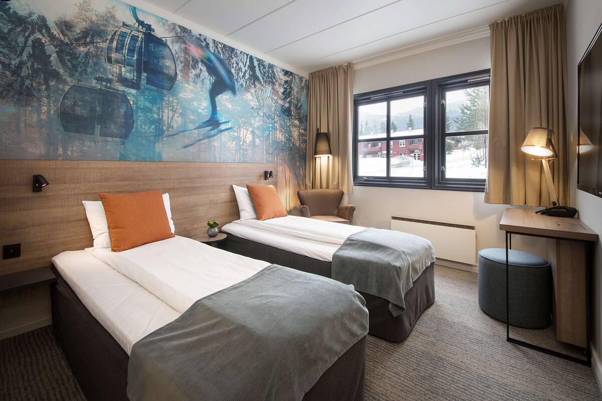 Habitación de hotel con dos camas, un ventanal con vistas, un escritorio con lámpara y un cuadro en la pared.