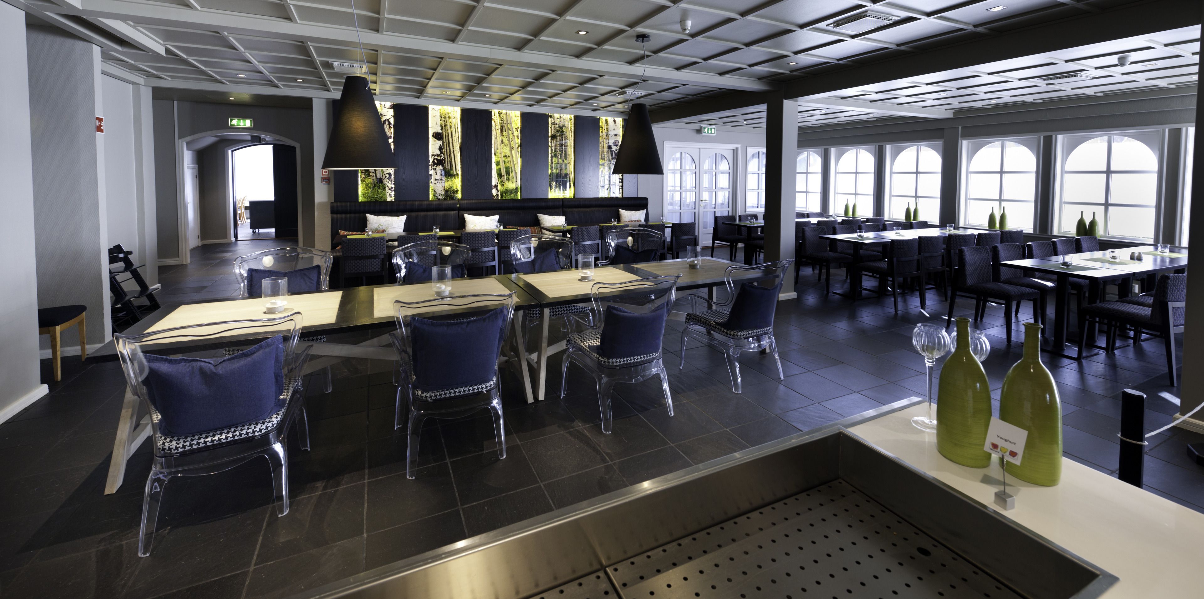 Un restaurant moderne doté d’un bar central, de chaises transparentes et de grandes fenêtres.