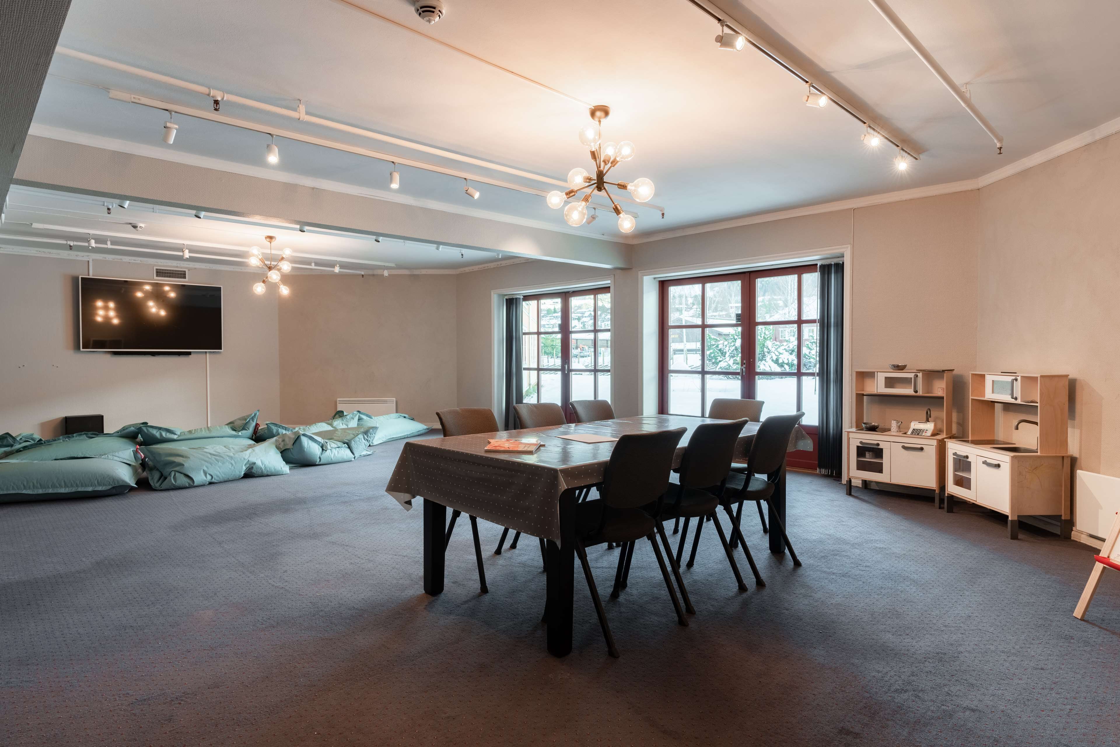 A spacious room with a large table, chairs, a television, and a kitchenette.