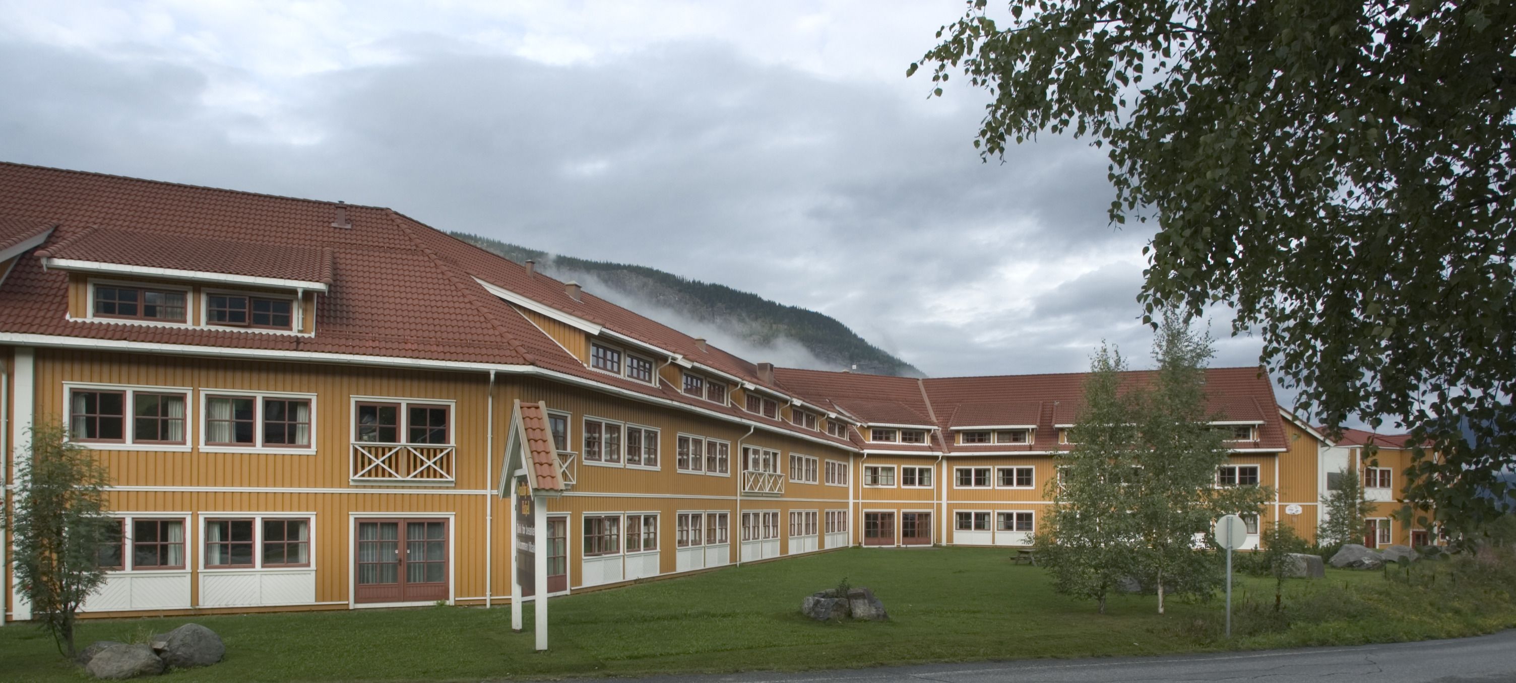 A multi-story building with a red-tiled roof, large windows, and a grassy courtyard.