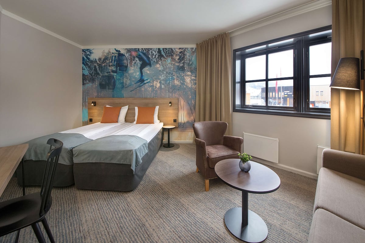 Habitación de hotel con cama, dos sillas, una mesita y un ventanal con cortinas.
